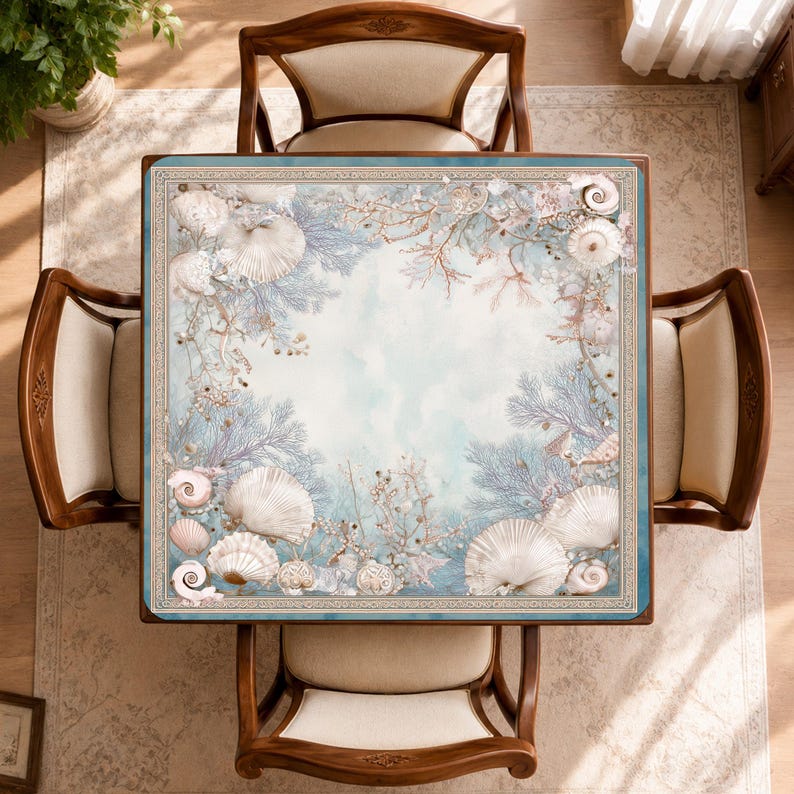 May include: A square table featuring a light blue surface decorated with a border of white seashells, coral, and sea fan illustrations. The table is surrounded by four wooden chairs with cream-colored upholstered seats, viewed from directly above.