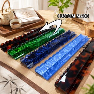 May include: Five elongated, rectangular acrylic display stands with scalloped edges, featuring marbled patterns in dark brown, emerald green, deep blue, light blue, and a second dark brown. The text CUSTOM MADE is visible above the stands.