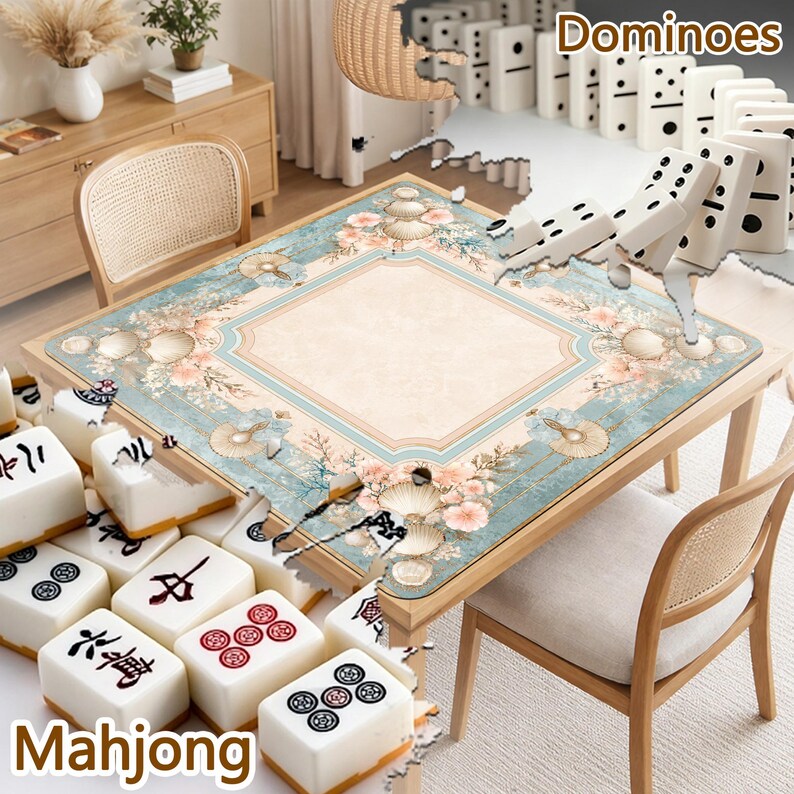 May include: A square game table mat featuring a light blue border with floral and seashell patterns surrounding a beige center. The mat is displayed with white Mahjong tiles in the foreground and a row of white dominoes in the background.