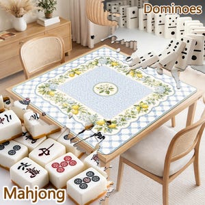 Puede incluir: Un tapete de juego cuadrado con un patr&oacute;n de celos&iacute;a en azul claro y blanco, bordeado por limones amarillos, hojas verdes y flores blancas. El centro muestra un motivo floral circular. El tapete est&aacute; rodeado de fichas de mahjong y domin&oacute;.