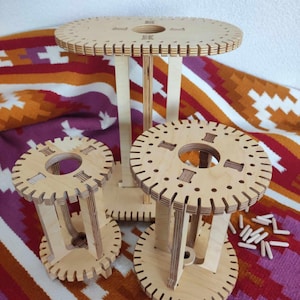 Puede incluir: Tres estructuras de madera de color claro en forma de bobina con plataformas circulares y ovaladas que presentan bordes dentados y orificios centrales. Las estructuras están hechas de madera contrachapada y vienen con varios pasadores de madera.