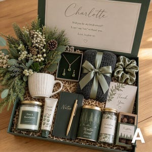 Könnte beinhalten: Eine Geschenkbox mit einem Strauß aus Grünpflanzen, einer weißen strukturierten Tasse, einem goldenen Halsketten- und Ohrringset, einem dunkelgrauen Strickteil mit salbeifarbenem Band, einem salbeifarbenen Haargummi, einer Kerze, Handcreme, einem Notizbuch, einem Stift, Badesalz und Trüffeln.