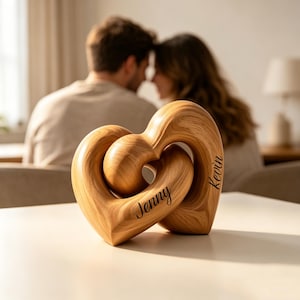 May include: A light brown wooden sculpture featuring two interlocking heart shapes. The smooth, polished wood displays a natural grain pattern. The name Jenny is engraved on the left heart, and the name Kevin is engraved on the right heart.