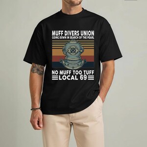 May include: Black t-shirt featuring a vintage-style graphic with the text "MUFF DIVERS UNION" and a diving helmet illustration. The design includes the phrase "GOING DOWN IN SEARCH OF THE PEARL" and "NO MUFF TOO TUFF LOCAL 69".