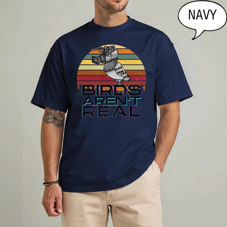 May include: Navy blue t-shirt featuring a retro sunset design with a pigeon wearing a video camera. The text "BIRDS AREN'T REAL" is displayed below the bird. The shirt is a solid navy color.
