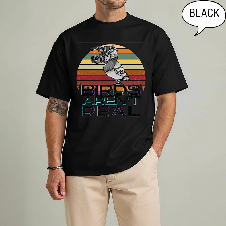 May include: Black t-shirt featuring a graphic of a pigeon with a video camera, set against a sunset design. The text "BIRDS AREN'T REAL" is displayed below the bird. The shirt is a classic crew neck style.