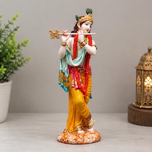 May include: A standing figurine of a deity playing a golden flute. The figure wears a yellow dhoti, a white and blue shawl, and a red garland. Adorned with gold-coloured jewellery, the figure has a peacock feather in the hair and stands on a base.