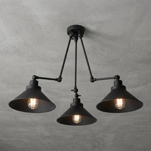 May include: A matte black ceiling light fitting featuring three adjustable arms extending from a central mount. Each arm holds a conical metal shade with an exposed Edison-style light bulb inside, providing downward illumination from the three heads.