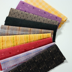May include: A fan-shaped arrangement of rectangular fabric swatches featuring various textures and patterns, including yellow plaid, purple houndstooth, black tweed, brown plaid, yellow wave, red houndstooth, lavender, and black textured weaves.