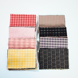 May include: A collection of eight rectangular fabric swatches arranged in two columns. The patterns include red, pink, and yellow gingham, a multi-colored plaid, and several black fabrics featuring white, purple, and gold grid or striped designs.