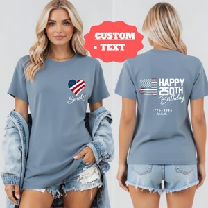 Könnte beinhalten: Ein staubblaues T-Shirt mit einem Herz im US-Flaggenmuster und dem Namen Emily auf der Vorderseite. Die Rückseite zeigt eine US-Flaggen-Grafik mit dem Text Happy 250th Birthday und 1776-2026 U.S.A. in weißer Schrift.