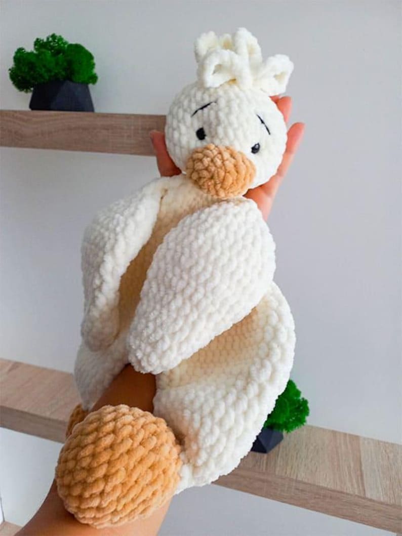 Pode incluir: Um brinquedo de pel&uacute;cia em croch&ecirc; com formato de ganso, feito de fio branco macio com acabamento texturizado e irregular. O ganso apresenta uma cabe&ccedil;a arredondada com olhos bordados em preto, um bico bege e p&eacute;s bege, com um pequeno tufo de fio.