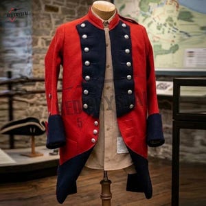 May include: A red wool coat with dark blue lapels, cuffs, and collar, featuring two vertical rows of silver-toned buttons. The coat is worn over a light tan button-down shirt. The garment has a high collar and long sleeves with dark blue cuffs.