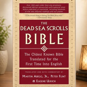 Op de afbeelding: Een boek getiteld "The Dead Sea Scrolls Bible" met een bordeauxrode kaft en gouden details. De kaft bevat tekst over de inhoud en vertaling van het boek. Het is een religieuze tekst.