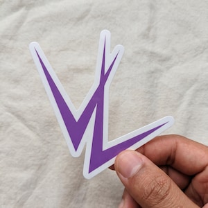 May include: A die-cut vinyl sticker featuring a stylized purple graphic design with sharp, angular lines that form a V-like shape with an extended vertical point. The sticker has a clean white border surrounding the purple shape, creating a high-contrast look.