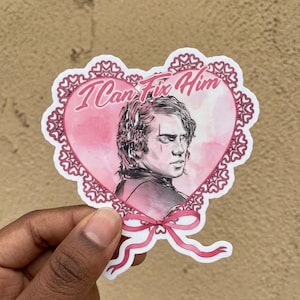 May include: A heart-shaped sticker with a pink watercolor background and a portrait of a person. The sticker has the text "I Can Fix Him" in a cursive font. The heart is outlined with a decorative lace pattern and a pink bow.