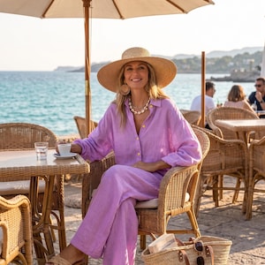 May include: A lavender linen button-down shirt and matching wide-leg trousers, paired with a wide-brimmed straw hat, a shell necklace, round woven earrings, and tan woven slide sandals, accompanied by a large straw tote bag with leather handles.