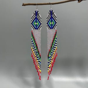 May include: A pair of beaded earrings with a geometric design. The earrings are primarily silver, with accents of blue, green, yellow, and red. The top portion features a diamond pattern, while the bottom has a fringe of beads.