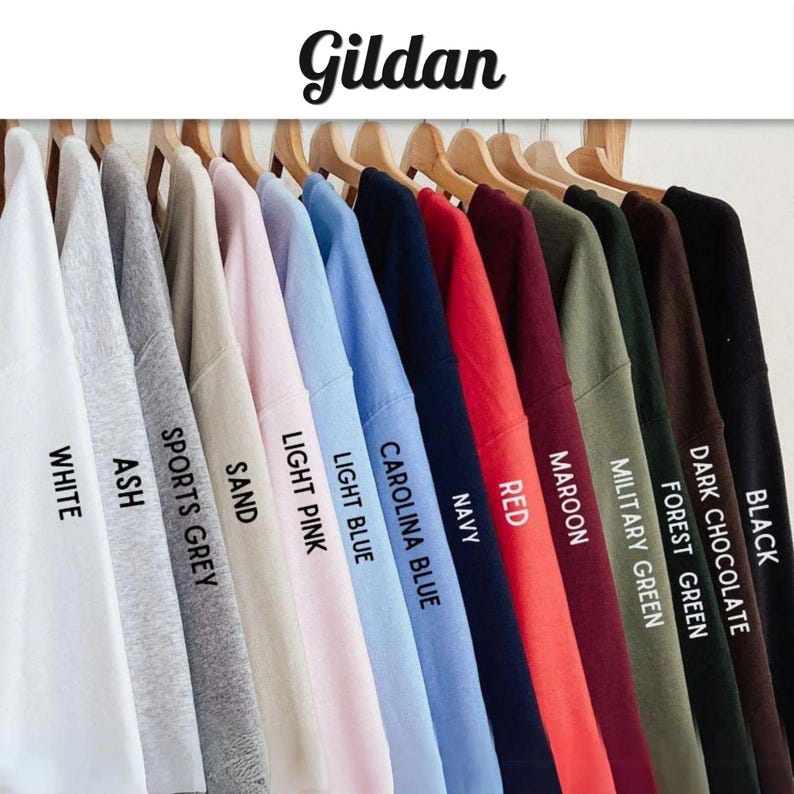 May include: A collection of Gildan crewneck sweatshirts hanging on wooden hangers, displayed in a color gradient. The colors include white, ash, sports grey, sand, light pink, light blue, carolina blue, navy, red, maroon, military green, forest green, dark chocolate, and black.