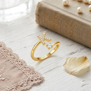 Peut inclure: Une bague ouverte dorée ornée d'une lettre K incrustée de petites pierres claires et d'une pierre ronde claire à l'autre extrémité. L'anneau porte l'inscription EST. 1920 gravée sur la surface extérieure, avec une finition métallique polie.