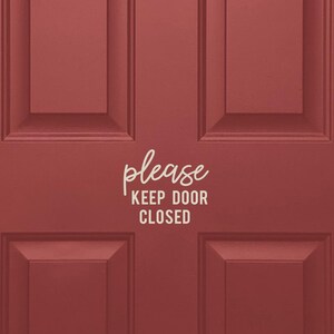May include: A red wooden door with a white door frame. A white sticker with the text "please keep door closed" is on the door.