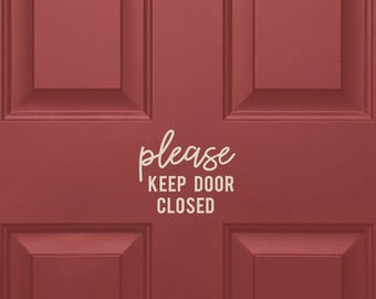 May include: A red wooden door with a white door frame. A white sticker with the text "please keep door closed" is on the door.