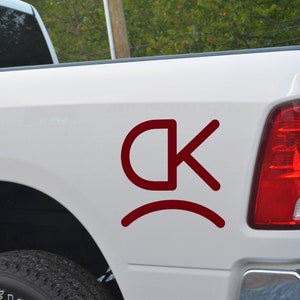 May include: A white pickup truck with a red "CK" logo and a red curved line underneath. The logo is on the back of the truck.