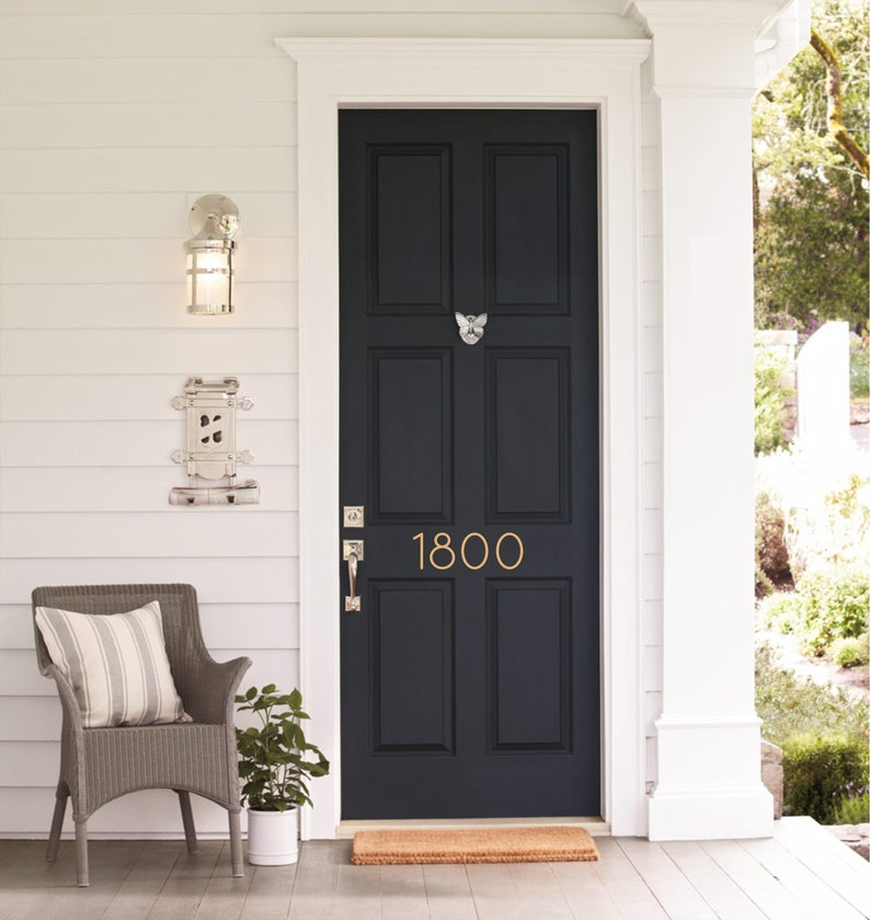 May include: A black front door with a gold door knocker and the number 1800 on it. The door is surrounded by white trim and a white porch.