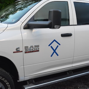 May include: White pickup truck with a blue logo on the side. The logo is a stylized arrow pointing upwards with an X underneath. The truck has a "RAM 3500 HEAVY DUTY" emblem on the front fender.