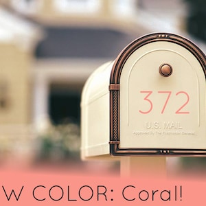 May include: A white mailbox with a copper colored trim and a coral colored house number "372". The mailbox has a U.S. Mail label and is approved by the Postmaster General.