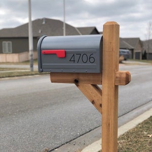 May include: A gray metal mailbox with a red flag and the number 4706 on the front. The mailbox is mounted on a wooden post.