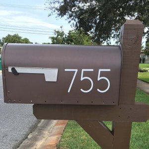 May include: A brown mailbox with a white number "755" on the front. The mailbox is mounted on a wooden post.
