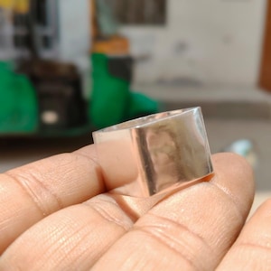 May include: A wide, polished silver-toned ring with a flat, square-shaped top surface and a smooth, reflective metallic finish. The band features a clean, geometric design with sharp edges and a uniform width, showcasing a bright, reflective luster.