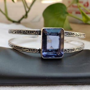 May include: A silver cuff bracelet featuring a large, rectangular, blue gemstone. The bracelet has an open design with two bands, each adorned with a decorative, repeating pattern. The gemstone is the focal point.