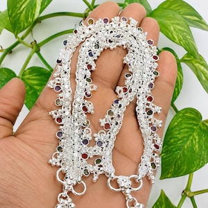 Peut inclure: Une paire de bracelets de cheville argentés présentant un travail du métal complexe et de petites pierres précieuses rondes et multicolores serties le long des chaînes. Chaque bracelet se termine par une breloque florale et des perles.