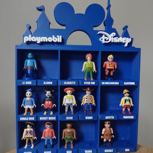 Peut inclure: Une étagère de présentation bleue imprimée en 3D avec une silhouette de château et des oreilles de Mickey Mouse au sommet. L'unité comporte quinze compartiments, chacun étiqueté avec un nom de personnage, abritant diverses figurines Playmobil Disney.