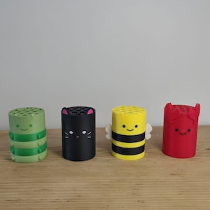 Peut inclure: Quatre porte-stylos cylindriques avec des sommets plats comportant plusieurs trous circulaires. Le premier est vert clair avec un motif de chenille, le deuxième est noir avec des oreilles de chat, le troisième est jaune avec des ailes d'abeille et le quatrième est rouge avec des pinces de crabe.