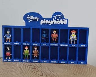 Puede incluir: Un expositor de plástico azul con el logotipo de Disney Playmobil en la parte superior. El soporte tiene dos filas de compartimentos individuales, cada uno etiquetado con el nombre de un personaje. Varias figuras de Disney están colocadas en los huecos.