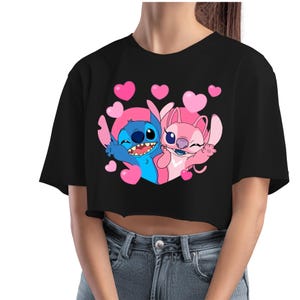 May include: Black crop top featuring a cartoon graphic of Stitch and Angel, surrounded by pink hearts. The blue Stitch and pink Angel are smiling and waving. The top is a short-sleeved, casual style.