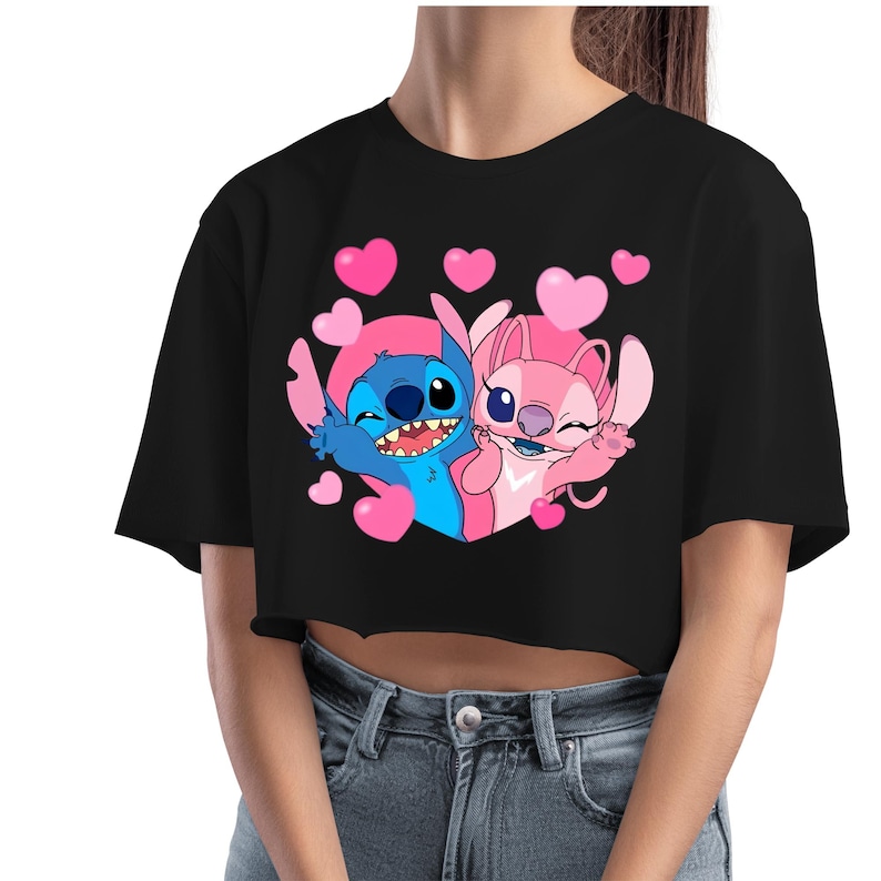 May include: Black crop top featuring a cartoon graphic of Stitch and Angel, surrounded by pink hearts. The blue Stitch and pink Angel are smiling and waving. The top is a short-sleeved, casual style.