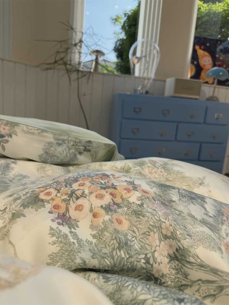 May include: A cream-colored duvet cover and pillowcase set featuring a repeating pattern of soft peach-colored flowers, green foliage, and intricate botanical illustrations. The fabric has a smooth texture with a detailed floral print throughout.