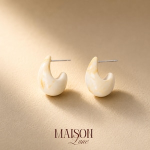May include: A pair of cream-colored hoop earrings with a smooth, marbled texture and subtle golden-brown swirls. Each earring features a silver-toned metal post and back closure. The text MAISON Lune is printed in dark brown at the bottom center.