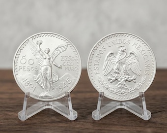 May include: Two silver-colored coins displayed on clear plastic stands. The left coin features a winged figure, the text 50 PESOS, 37.5gr ORO PURO, and the years 1821 and 1945. The right coin shows an eagle, the text ESTADOS UNIDOS MEXICANOS.