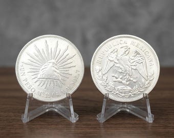 May include: Two silver Mexican one peso coins from 1904 displayed on clear plastic stands. The left coin features a Phrygian cap with rays and the word LIBERTAD. The right coin shows an eagle perched on a cactus with REPUBLICA MEXICANA text.