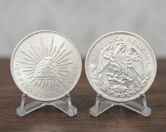 May include: Two silver Mexican one peso coins displayed on clear plastic stands. The left coin features a Phrygian cap with rays and the text UN PESO Z 1901 F Z.902.7. The right coin shows an eagle perched on a cactus with REPUBLICA MEXICANA.
