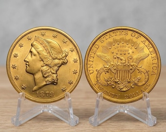 May include: Two gold-colored coins displayed on clear plastic stands. The left coin features a profile of Lady Liberty with the year 1879. The right coin shows an eagle with a shield, the text United States of America, and Twenty Dollars.