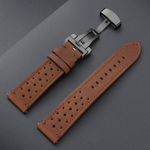 May include: Brown leather watch strap with a black clasp. The strap features a perforated design and visible stitching. The watch band is shown against a dark gray background.