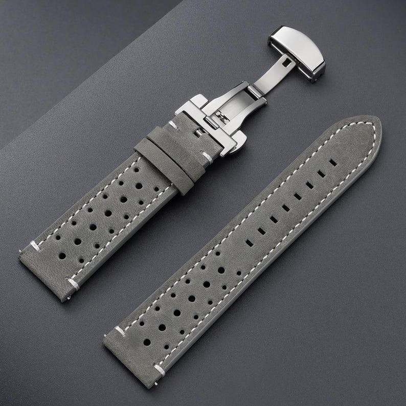 May include: Gray leather watch strap with white stitching and a stainless steel clasp. The strap features a perforated design and is shown against a dark gray background. The watch band is a replacement part for a watch.