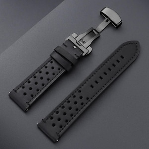 May include: Black leather watch strap with a black metal clasp. The strap has a perforated design and is shown in two pieces, with the clasp open. The background is a dark gray surface.