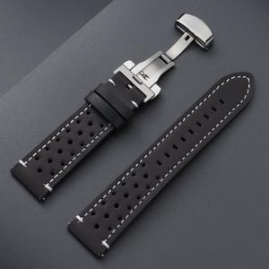 May include: Black watch strap with white stitching and a stainless steel clasp. The strap features a perforated design for breathability and a secure fit. The watch band is made of a durable material.
